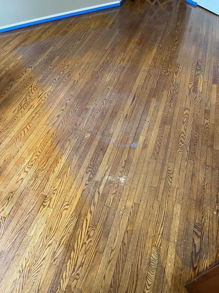 A dull, stained, discolored hardwood floor being prepped for refinishing by ReCoat Revolution.