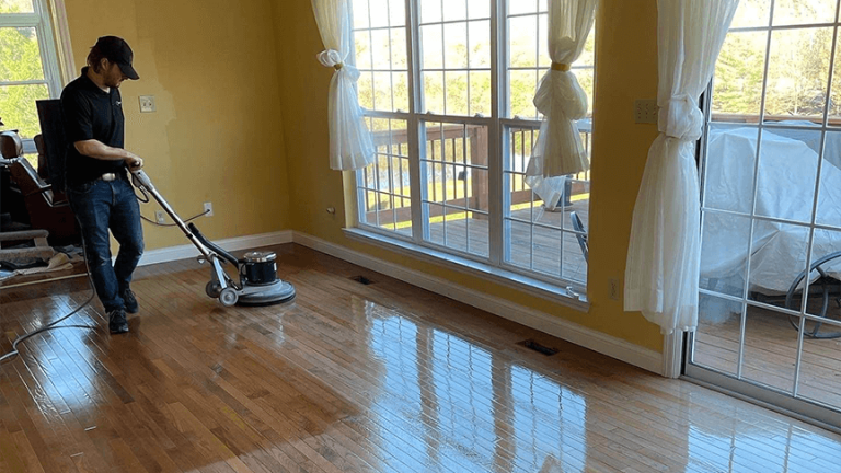 A ReCoat Revolution technician buffing an engineered hardwood floor in a residential living space to remove built up grime before refinishing.