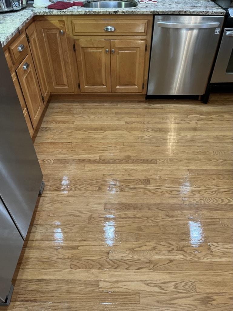 A restored, glossy, stain-free hardwood floor in a residential kitchen after refinishing by ReCoat Revolution.