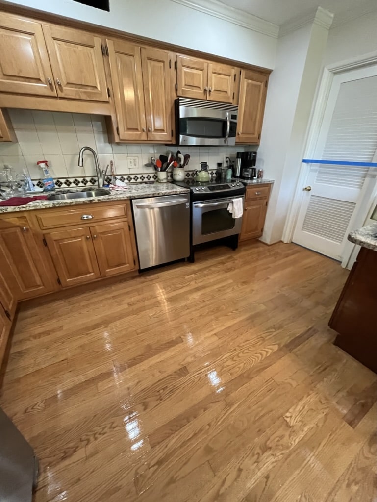 The glossy, stain-free hardwood floor in a residential kitchen after being refinished by ReCoat Revolution.
