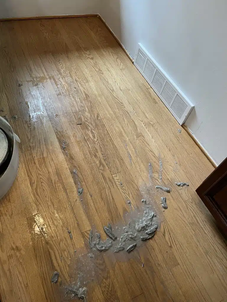 A hardwood floor having the acrylic wax removed by ReCoat Revolution. A pile of wet, dirty gray buildup sits on the floor, showcasing what's been removed so far.