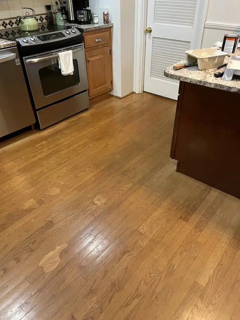 A dull, stained, and scuffed hardwood floor in a residential kitchen before being refinished by ReCoat Revolution.