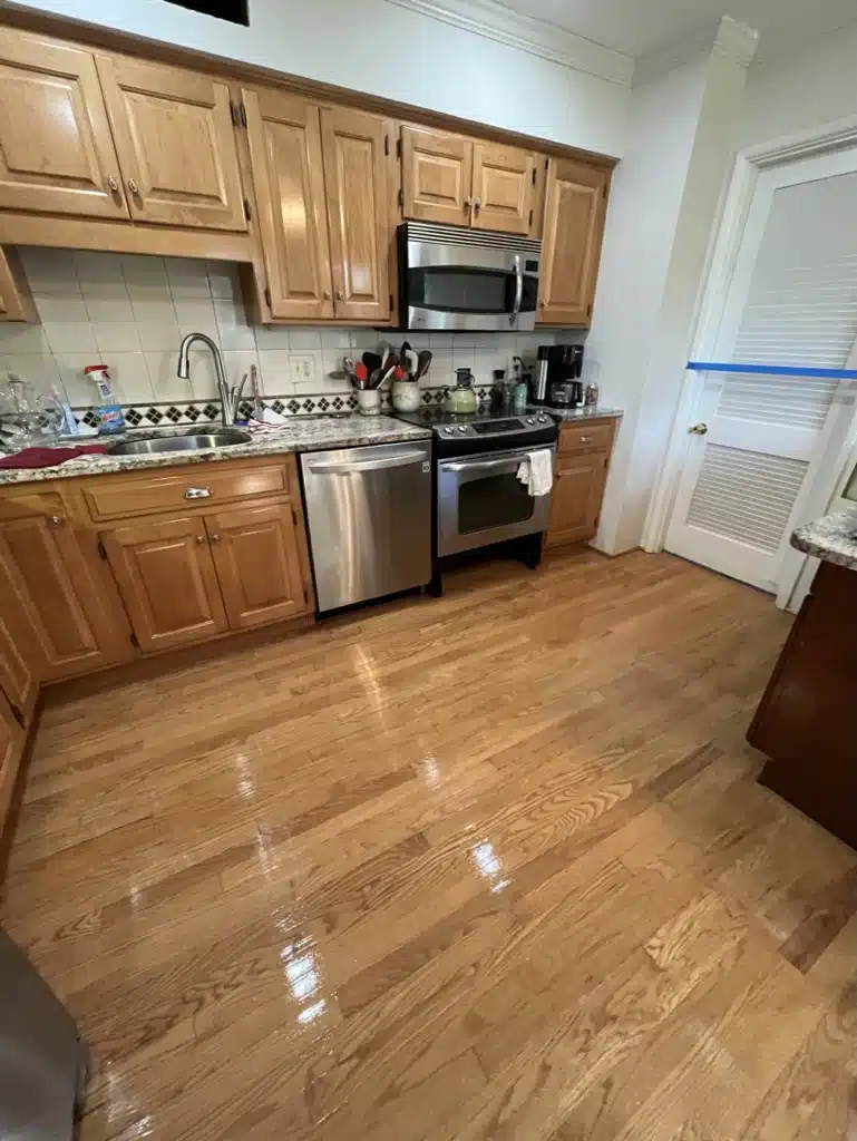 The glossy, stain-free hardwood floor in a residential kitchen after being refinished by ReCoat Revolution.