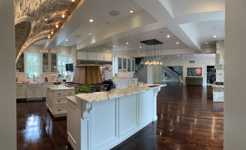 A large, open concept kitchen and living space in a home with dark hardwood floors, refinished with a semi-gloss by ReCoat Revolution.