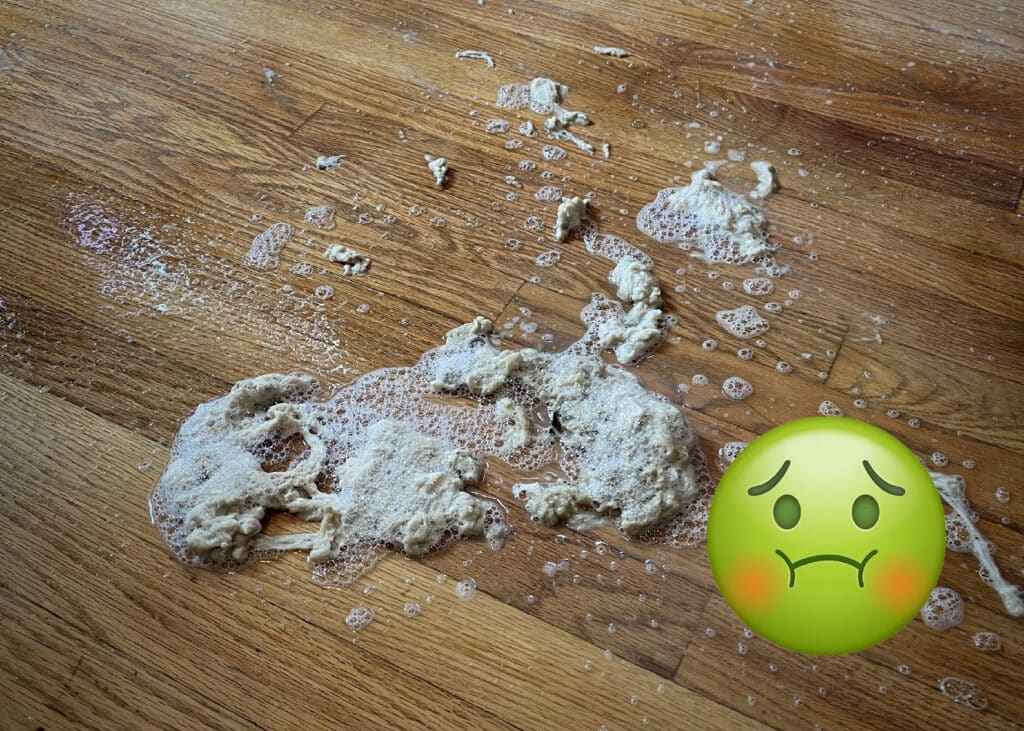 Close-up showing a pile of gunky build-up surrounded by bubbles that cleaning product Rejuvenate leaves on floors that has been removed by ReCoat Revolution, accompanied by a sick-faced emoji in the lower right-hand corner.