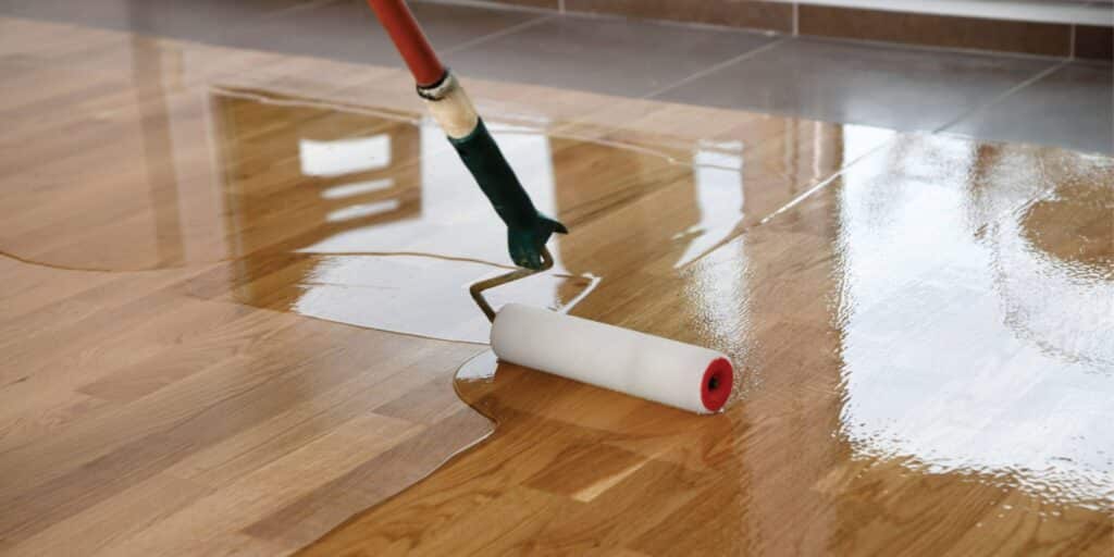 An attempt at doing floor resurfacing yourself with a long foam roller and compound being spread across a wood floor.