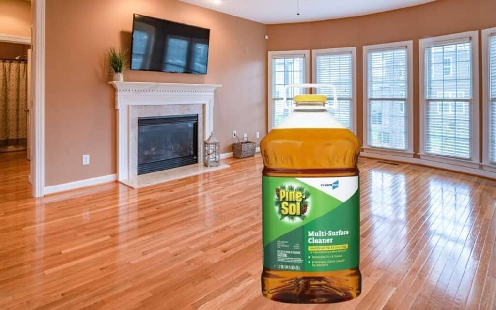An image of a large residential living room with all furniture cleared away for full hardwood floor cleaning with a bottle of Pine Sol displayed in front.