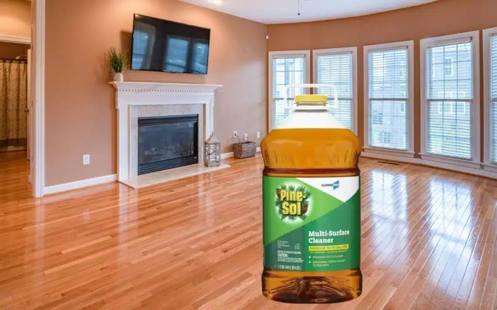 An image of a large residential living room with all furniture cleared away for full hardwood floor cleaning with a bottle of Pine Sol displayed in front.