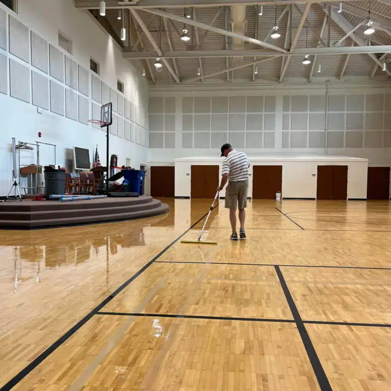 A ReCoat Revolution employee spreading a new, glossy finish on the refinished wood gym floor at the Central Institute for the Deaf.