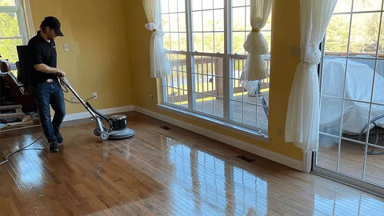 A ReCoat Revolution technician buffing an engineered hardwood floor in a residential living space to remove built up grime before refinishing.