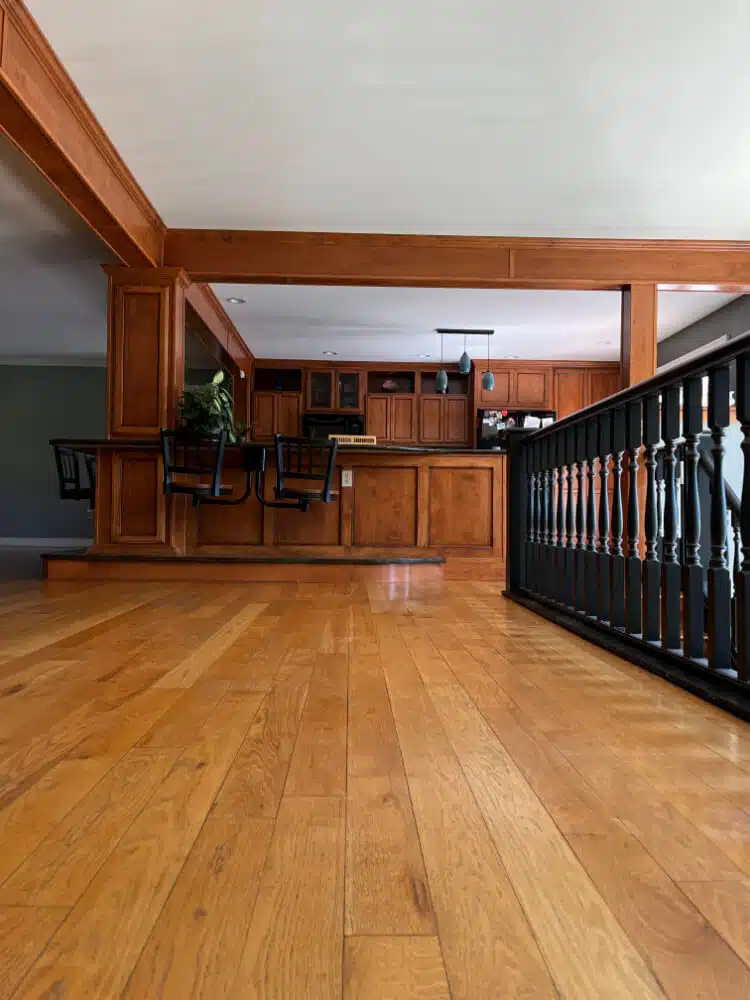 An image from floor-level of the hardwood floor after refinish work by ReCoat Revolution in the Jackson residence, looking toward the wood-framed kitchen with built-in barstools.