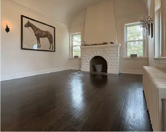 A room within an older home with painted stone fireplace, radiator heating, and dark wood floors that have been refinished by ReCoat Revolution.