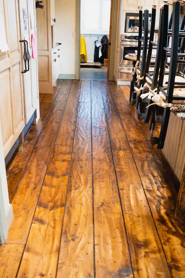 The result of refinishing work by ReCoat Revolution of a natural, hand-sawn wood floor in a residential kitchen.