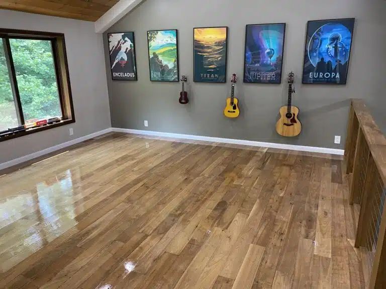 A showcase of a natural wood floor after refinishing by ReCoat Revolution with a high-gloss finish in a residential space with artistic posters and musical instruments on the wall.