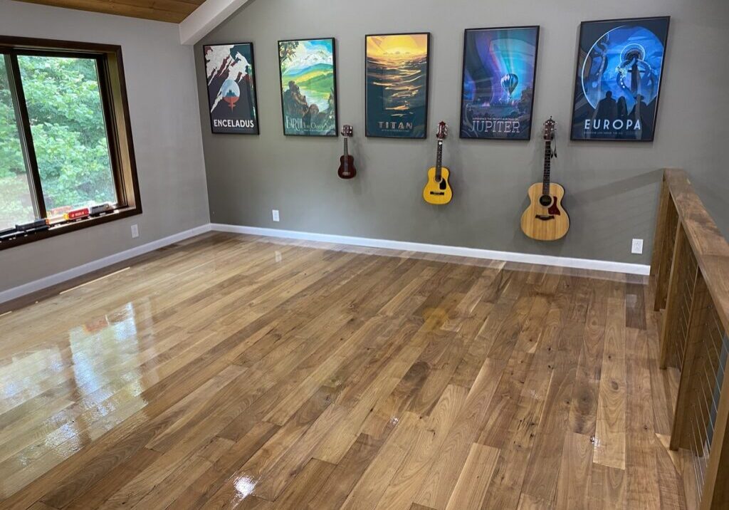 A showcase of a natural wood floor after refinishing by ReCoat Revolution with a high-gloss finish in a residential space with artistic posters and musical instruments on the wall.