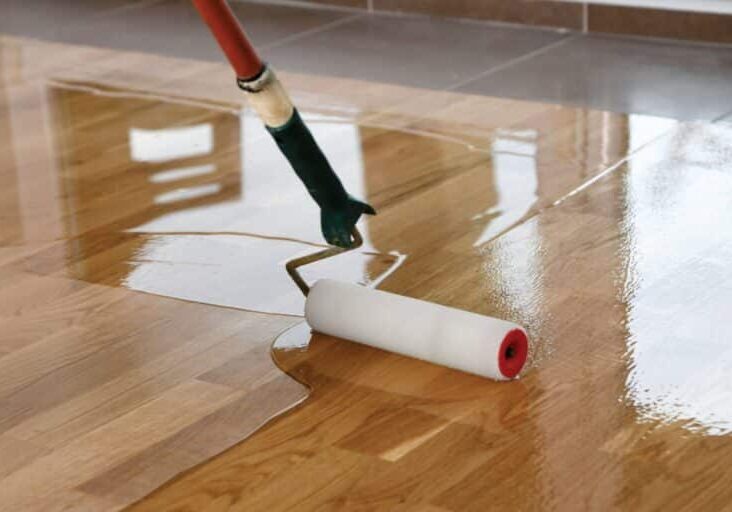 An attempt at doing floor resurfacing yourself with a long foam roller and compound being spread across a wood floor.