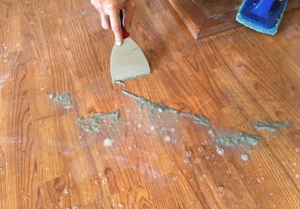 A close-up of the dirty acrylic wax build-up being scraped off after loosened with a solution as performed by ReCoat Revolution.