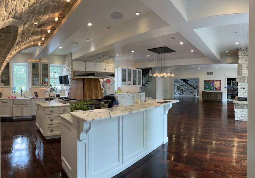 A large, open concept kitchen and living space in a home with dark hardwood floors, refinished with a semi-gloss by ReCoat Revolution.