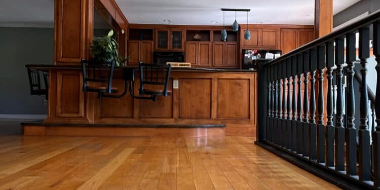 An image from floor-level of the hardwood floor after refinish work by ReCoat Revolution in the Jackson residence, looking toward the wood-framed kitchen with built-in barstools.